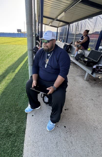 Coach holding a tablet beside a softball field